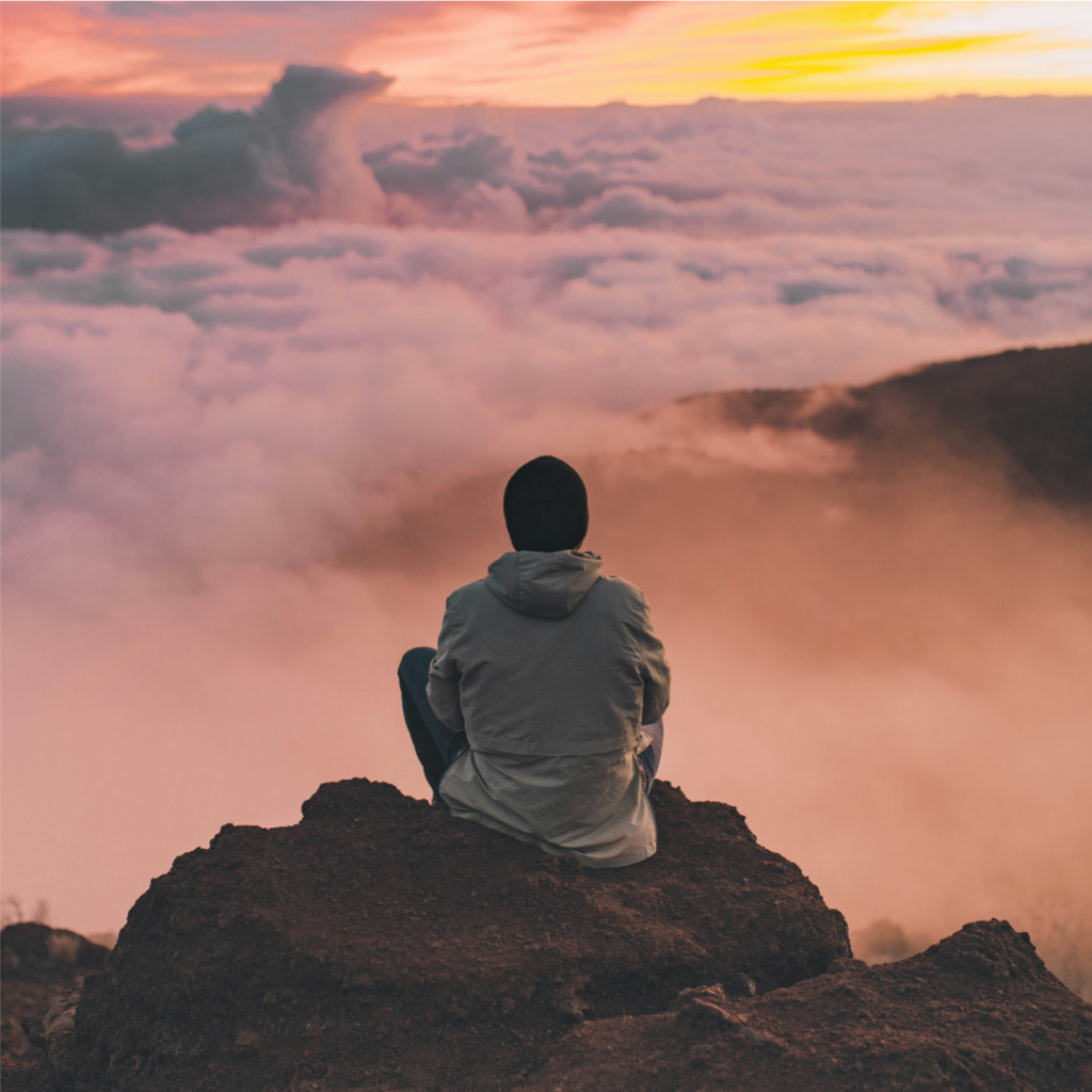 Un homme assis au sommet d’une montagne regardant les nuages.