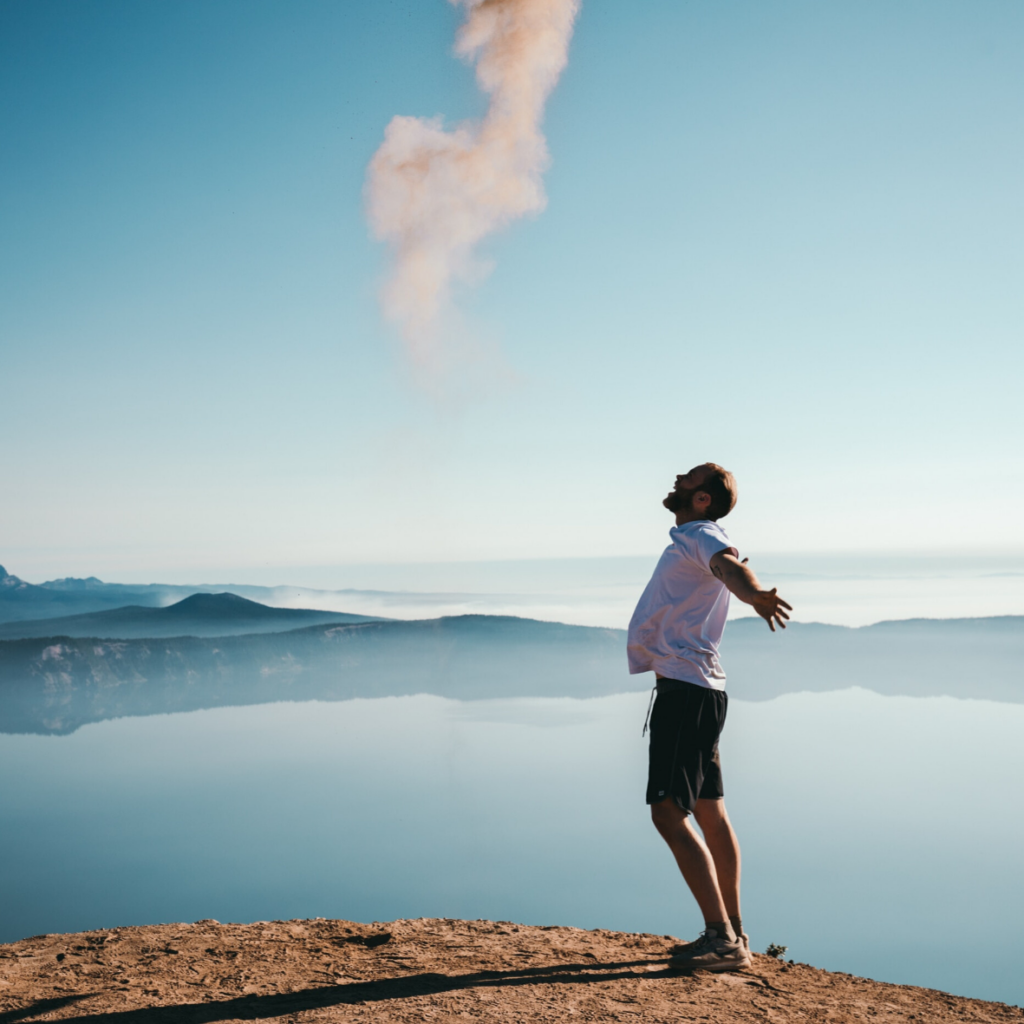 Un homme debout au sommet d’une montagne avec de la fumée sortant de sa bouche.